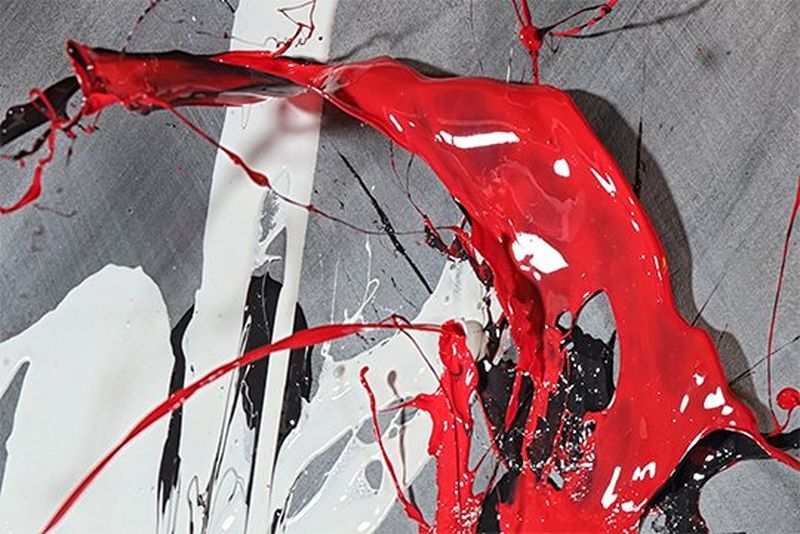 Red and white paint being thrown through the air onto a grey sheet. 