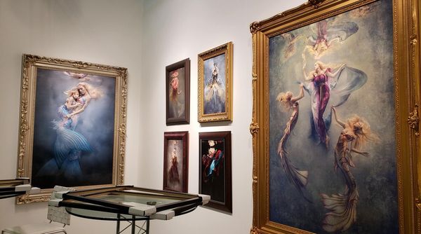 Fine art style images in ornate frames hang on the wall of a gallery.