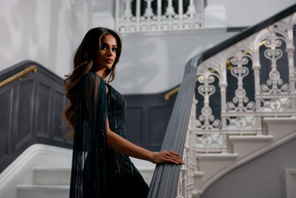 A woman in a green sequinned dress looks back over her shoulder as she climbs a staircase. 