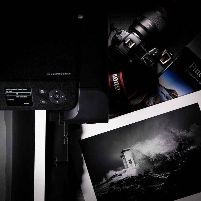 A Canon camera next to a Canon printer and a selection of black-and-white prints.