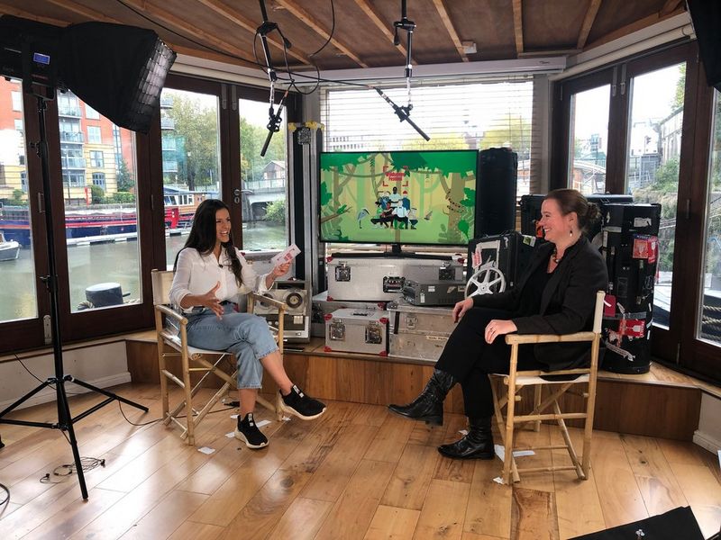 Two presenters sit on deck chairs inside a restored barge that is being used as a production set.