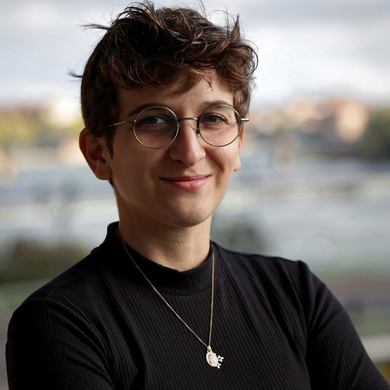 A headshot of Valentine Chapuis wearing a black sweater, a pendant and glasses. 