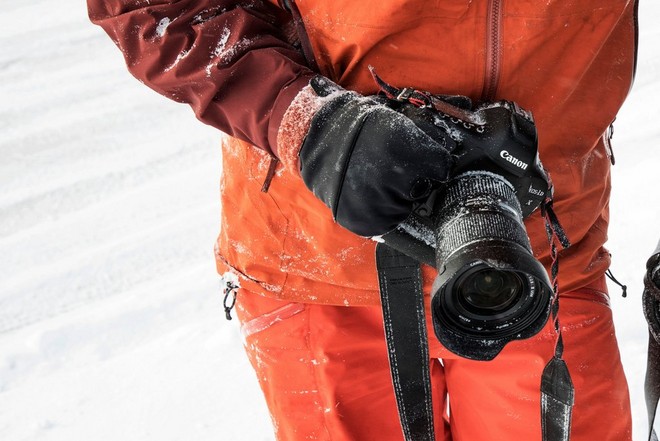 Una mano guantata sorregge una fotocamera Canon dotata di paraluce, per proteggere l'obiettivo dalle condizioni invernali.