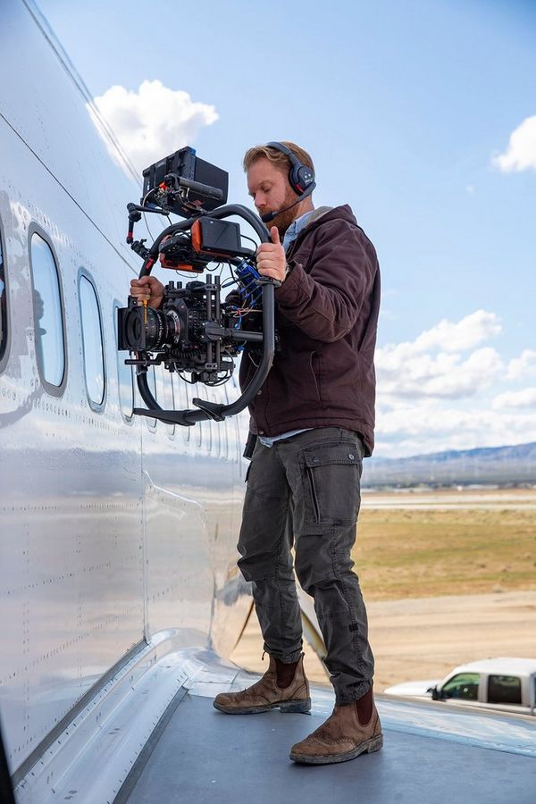 Steve Holleran with the Canon EOS C300 Mark III, standing on the wing of a plane.
