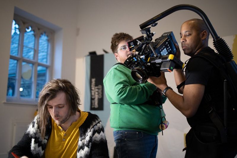 Three men shoot a scene for a corporate video using a Canon EOS C700 FF camera.