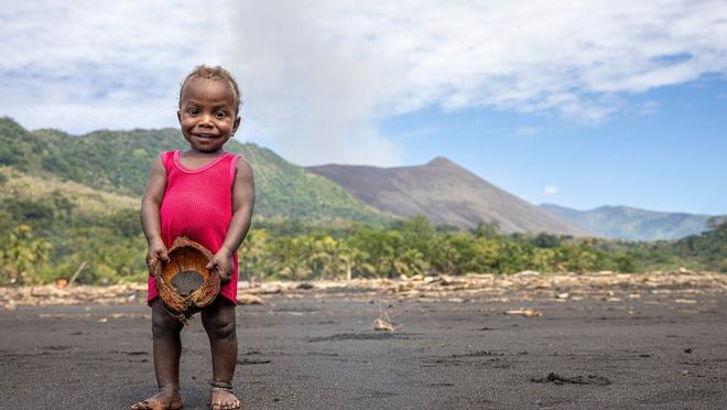 A portrait of a young child in a bright red dress with a smoking volcano in the background, taken on a Canon EOS R5 by Ulla Lohmann