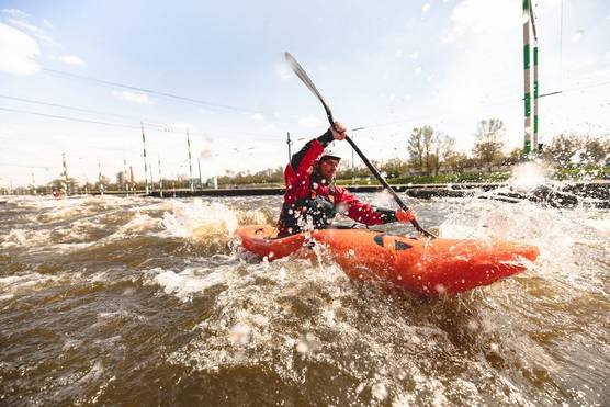 A person in an orange kayak paddling through fast-moving water.
