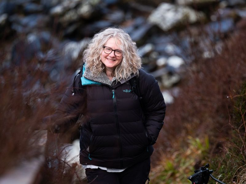 Filmmaker Heather Hughes stands against a rural backdrop, smiling at the camera.