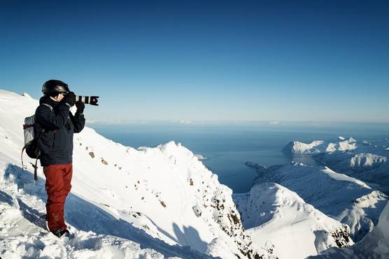 A man taking a photograph with a Canon camera and lens on the side of a snowy mountain. 