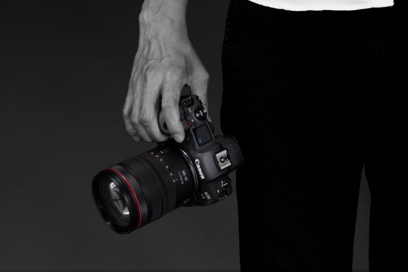 Une main d'homme tient de manière décontractée un Canon EOS R5 équipé d'un objectif Canon RF 24-105mm F4L IS USM.