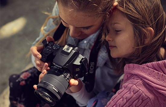A mother and daughter look at the back of a Canon EOS 250D.