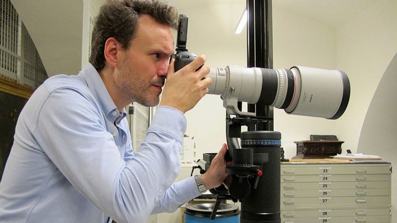 Un hombre sostiene una cámara Canon con un objetivo profesional y hace una foto.