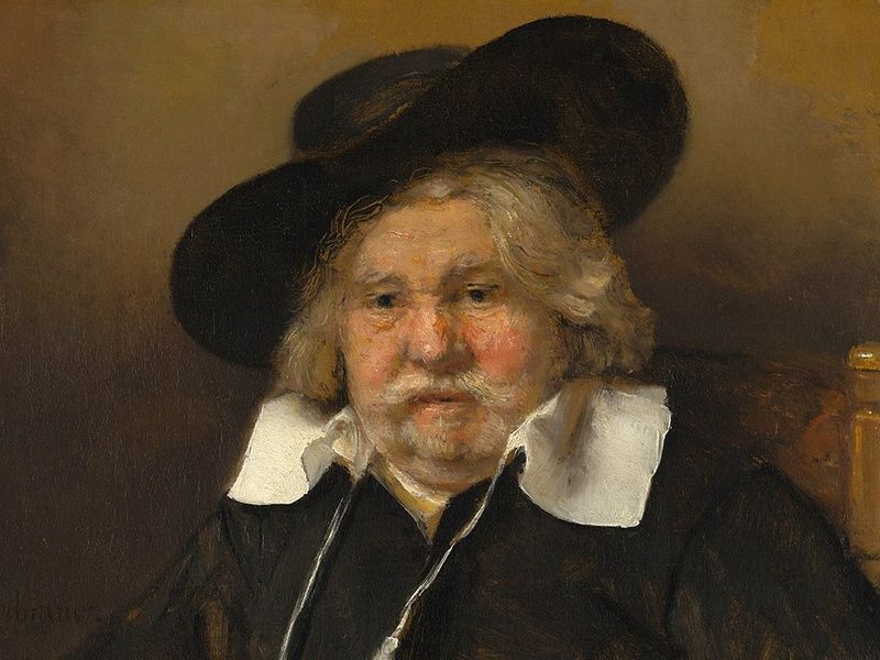 Rembrandt’s Portrait of an Elderly Man with long gray hair, gray beard, and moustache, wearing a large black hat, white shirt collar, and black clothing. (Copyright: Mauritshuis collection, The Hague).