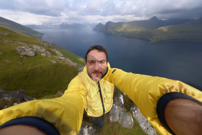 Joel Santos scatta un selfie con una fotocamera Canon collegata a un obiettivo Canon RF 10-20mm F4L IS STM, dietro di lui sono visibili un lago e delle colline.