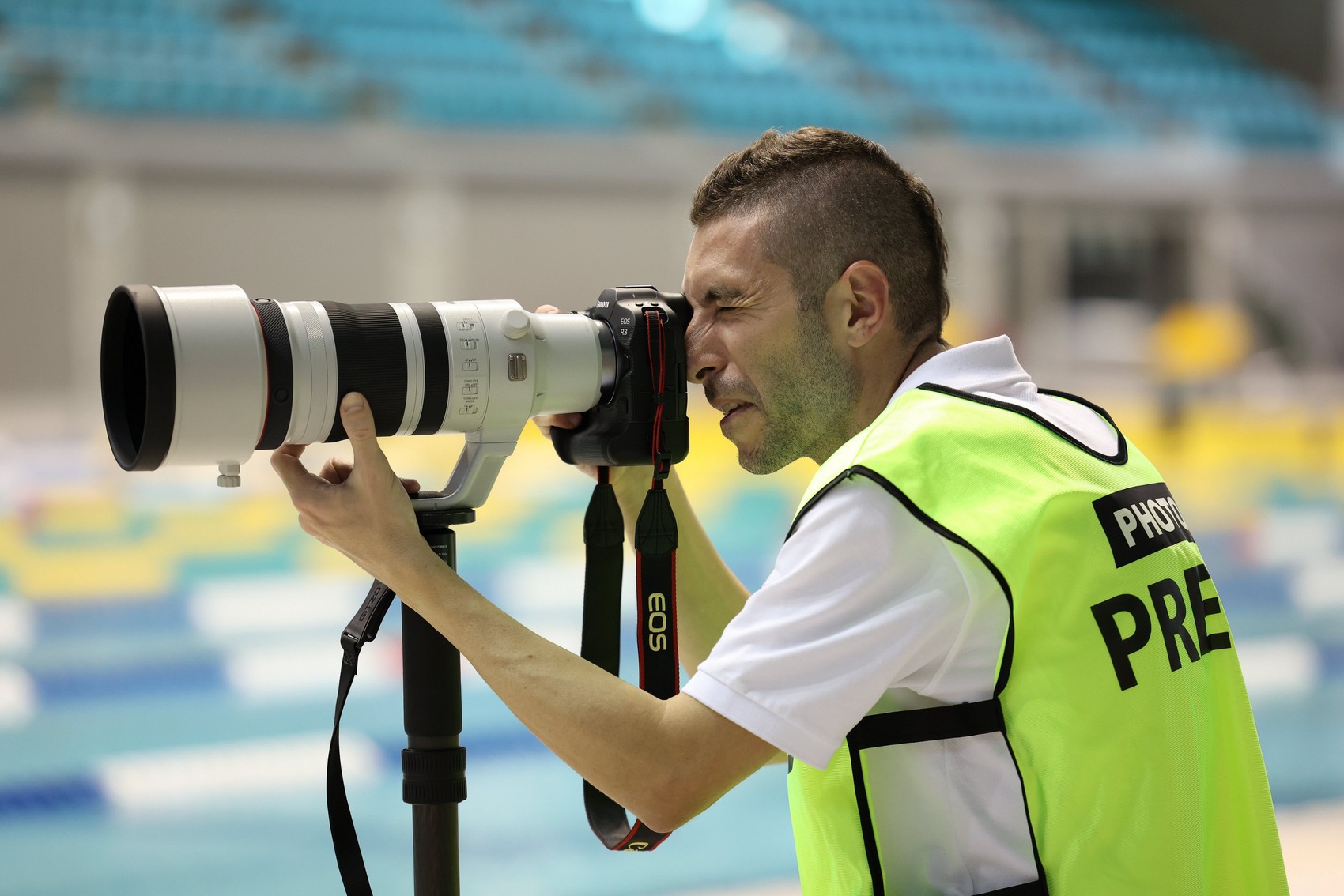A photographer wearing a high-visibility jacket uses a Canon EOS R3 with RF 100-300MM F2.8L IS USM lens attached on a monopod.