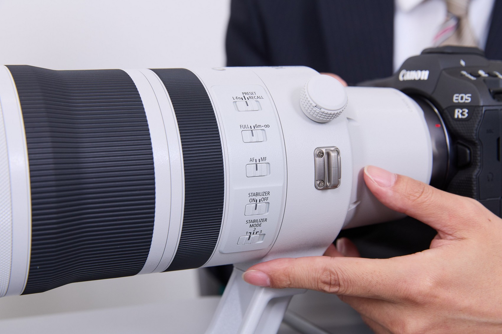 A hand poised alongside the controls on the side of barrel of the RF 100-300MM F2.8L IS USM.