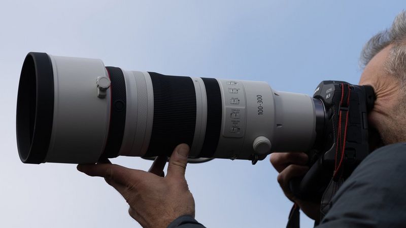 Person holding a Canon camera with a zoom lens.