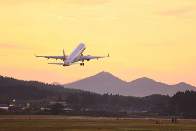 A plane taking off at dusk, the hills and mountains in the distance silhouetted against a yellow sky.