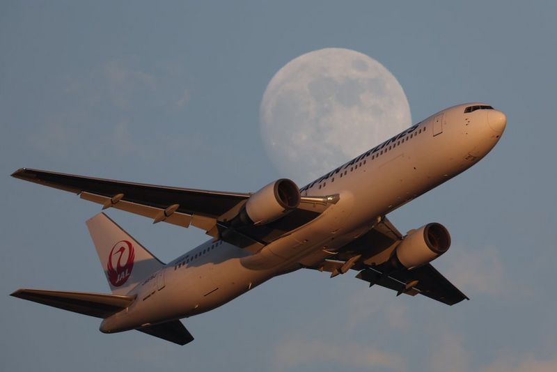 A commercial airliner in flight, with the moon looming large in the background.