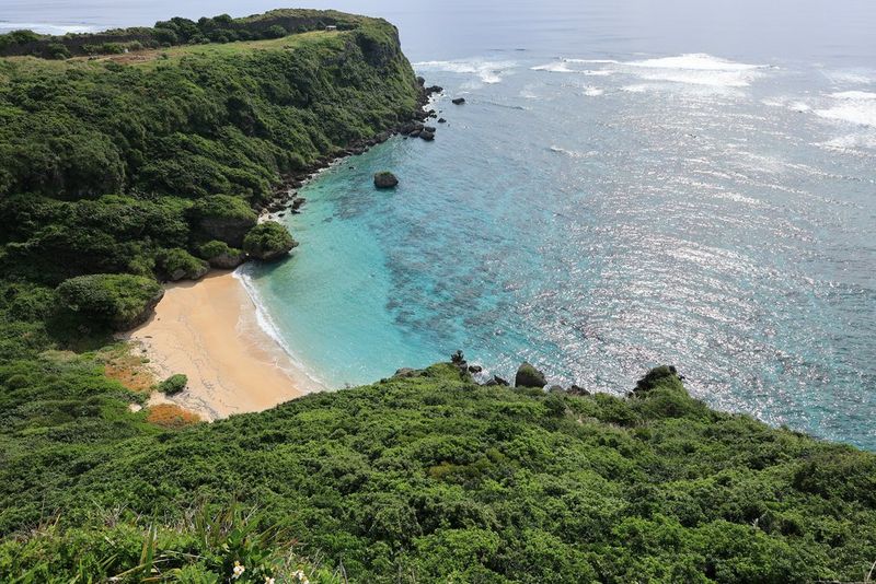 A landscape image taken from above of a beautiful bay encircled by green foliage and turquoise-blue water.