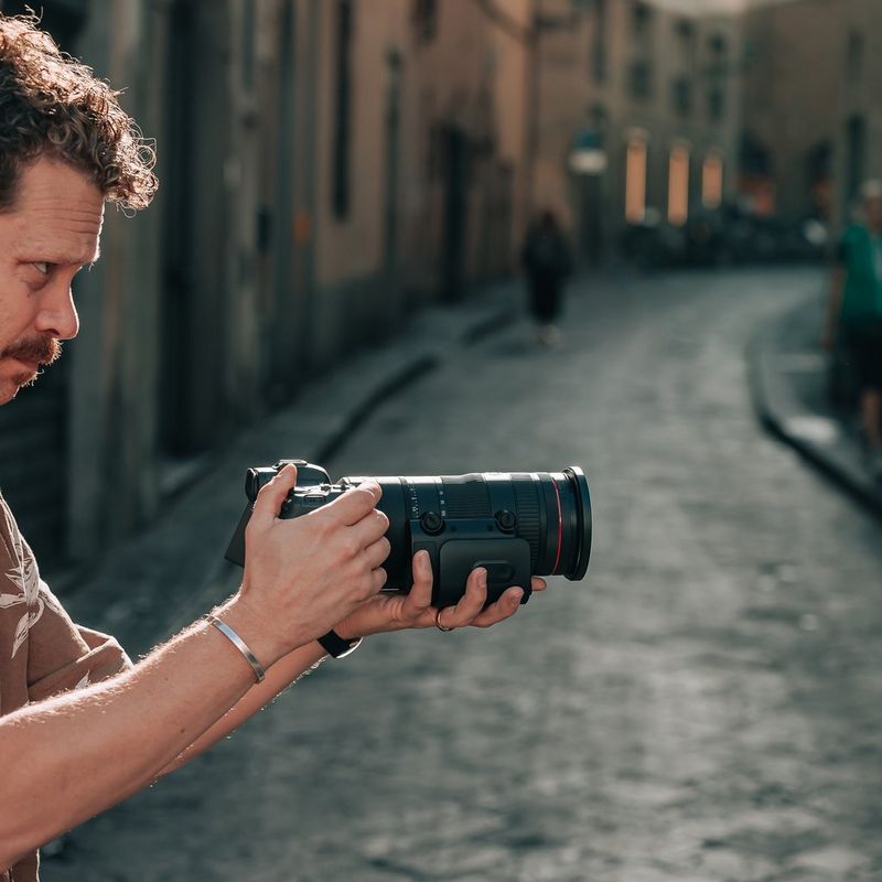 A man standing on an Italian street holds up a camera with a Canon RF 24-105mm F2.8L IS USM Z lens.