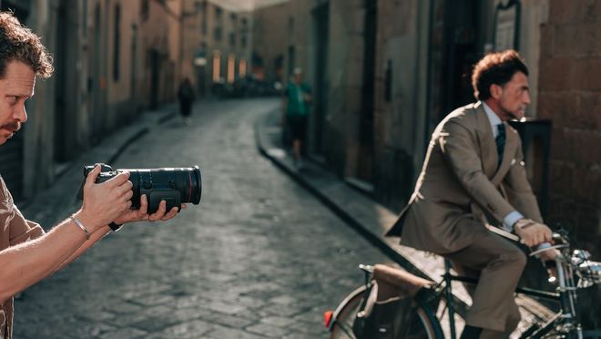 Een man fotografeert een fietsend model in pak in de straten van Florence met een Canon RF 24-105mm F2.8L IS USM Z-lens