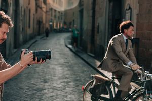 A man photographs a besuited model riding a bicycle through the streets of Florence with a Canon RF 24-105mm F2.8L IS USM Z lens.