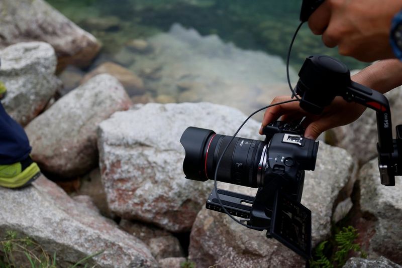 A close-up of a Canon camera with a Canon rf-24mm-f1.4l-vcm lens on a gimbal arm being used on a rocky seashore.