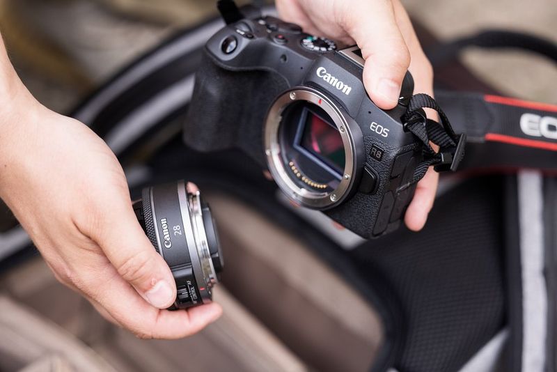 A user holds a Canon EOS R8 in one hand and an RF 28mm F2.8 STM lens in the other.