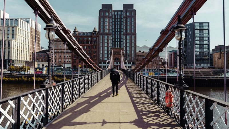 Street photographer Andres McNeill captures a street photography image of a figure walking across a long suspension bridge.