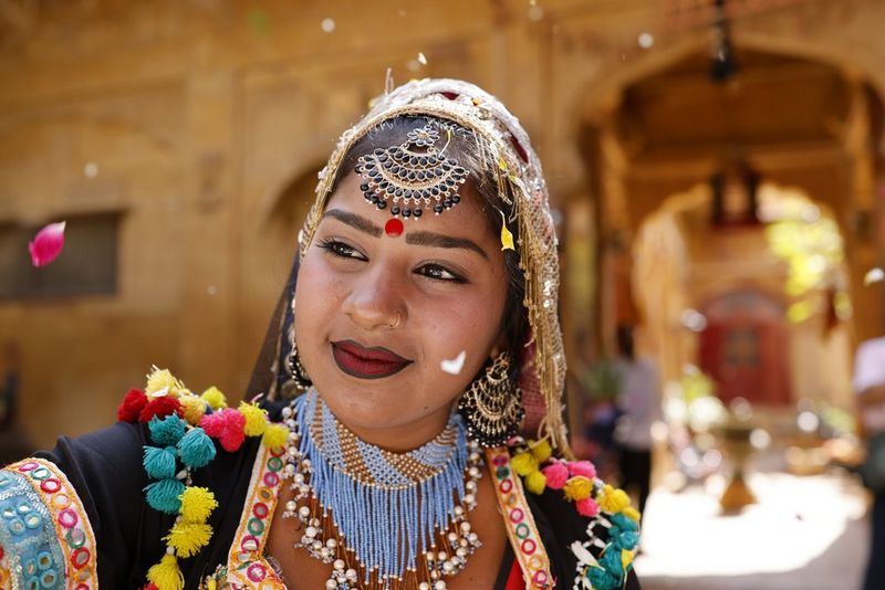 A portrait of a dancer wearing brightly coloured Indian traditional dress, with a large stone building out of focus in the background, taken with a Canon RF 35mm F1.4L VCM lens. 