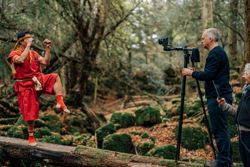 A man filming a martial arts practitioner with a Canon EOS R5 and a Canon RF 5.2mm F2.8L Dual Fisheye lens fixed to a boom arm mounted on a tripod.