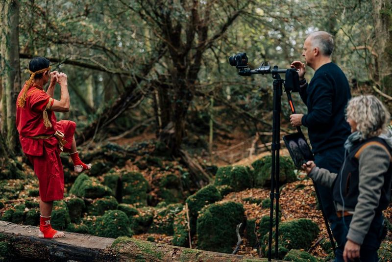 DoP Richard Stegmann and VR Director Mary Matheson filming a martial arts practitioner with a Canon EOS R5 and a Canon RF 5.2mm F2.8L Dual Fisheye lens mounted on a tripod in the middle of a forest.