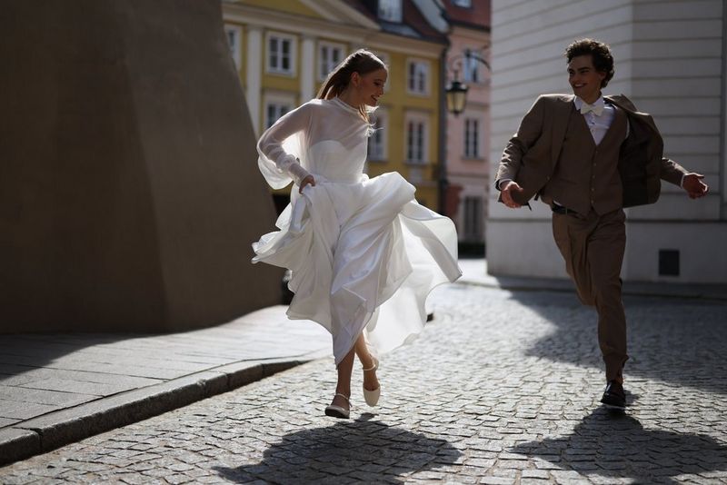 A bride and groom running in a cobbled street with colourful old buildings in the background, photographed with a Canon RF 50mm F1.4L VCM lens.