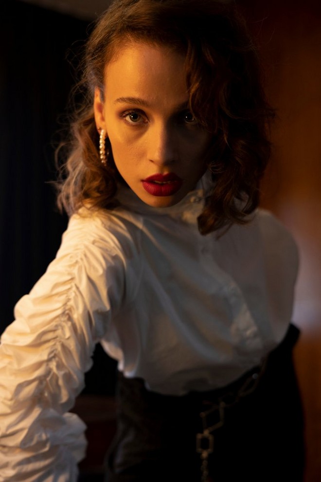 A model in a white frilly blouse poses in low light.