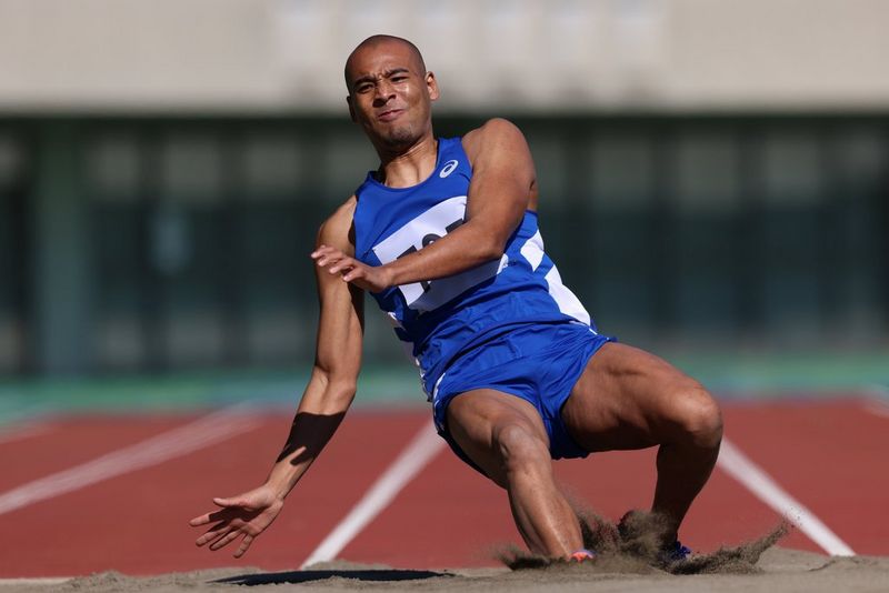 Un athlète atterrit lourdement dans un bac à sable après un saut sur une piste d'athlétisme.