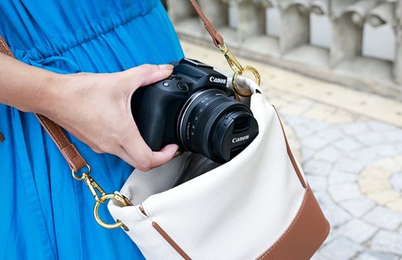 A hand pulling a Canon camera with a Canon RF-S 10-18mm F4.5-6.3 IS STM lens attached out of a handbag.