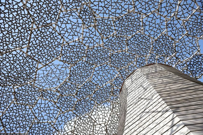 The roof of a building, made up of metal hexagons with crisscrossing wires, taken from below on a sunny day.