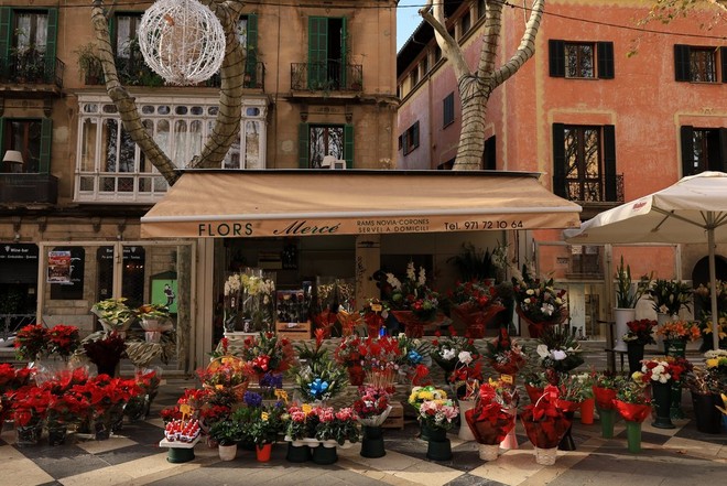 A small flower shop on a Spanish street. Outside the shop, multiple bouquets are on display.