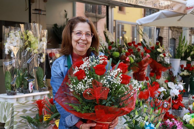 صورة لبائع زهور مبتسم يحمل باقة من الورود الحمراء.