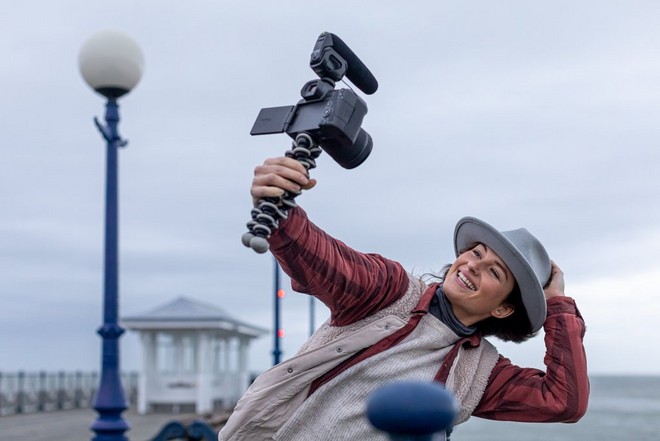 Un fotografo si riprende su un molo battuto dal vento, utilizzando una fotocamera Canon a cui è collegato un microfono con parabrezza.