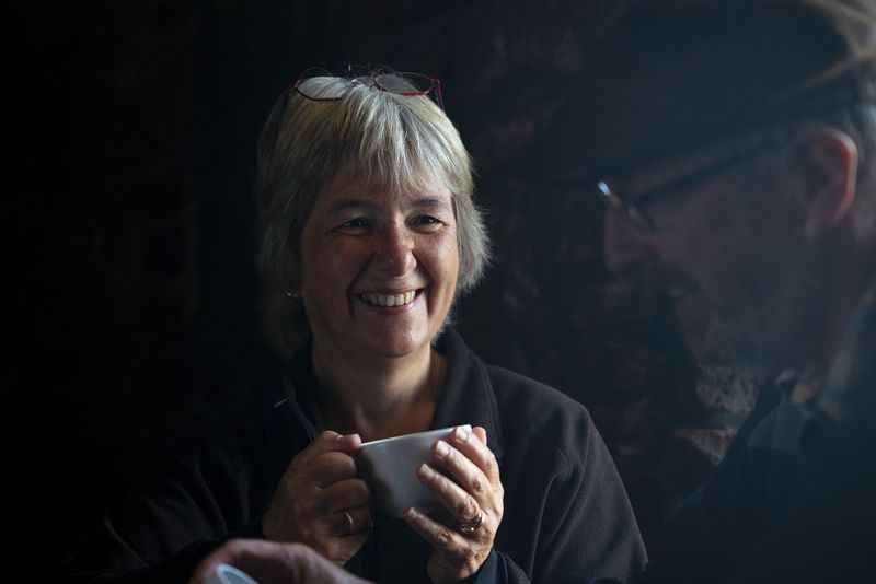 A low-light portrait of a woman holding a cup and smiling at her companion.