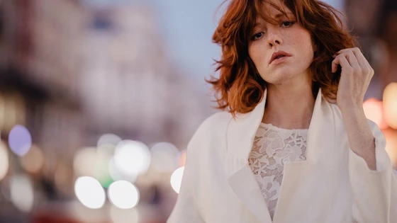 A portrait of a model in a white jacket in front of a busy but blurred street taken by Félicia Sisco with a Canon RF 85mm F1.2L USM lens.