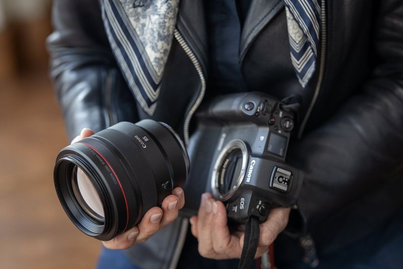 Человек держит в одной руке камеру Canon, а в другой — объектив RF, словно собираясь установить его на камеру.