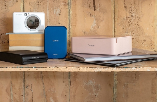 A collection of compact Canon photo printers in various colours on a wooden shelf.