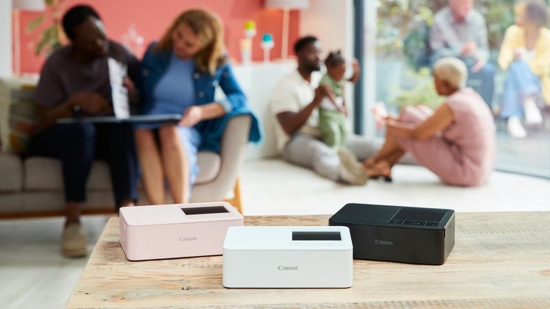 SELPHY CP1500 in all three colours on a table with a couple and a family in the background.