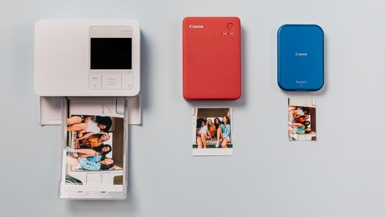 Canon Zoemini and SELPHY range printers placed with some books on a wooden shelf.