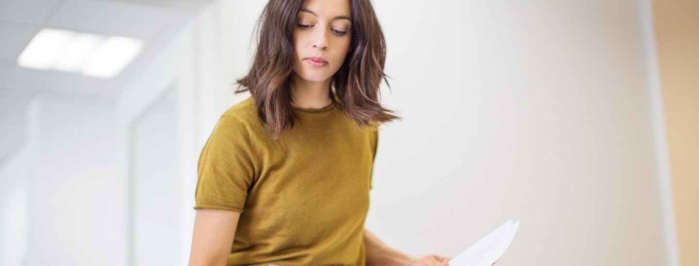 Woman with brown hair and wearing a yellow top carries paper in both hands