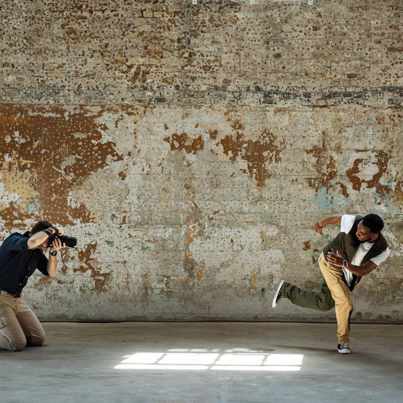 Photographer David Newton crouches down to capture a dancer mid-move against a distressed concrete wall.