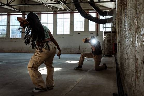 A photographer crouches down to photograph a woman dancing in a warehouse, his face obscured by the flare created as the Canon Speedlite EL-5 fires.